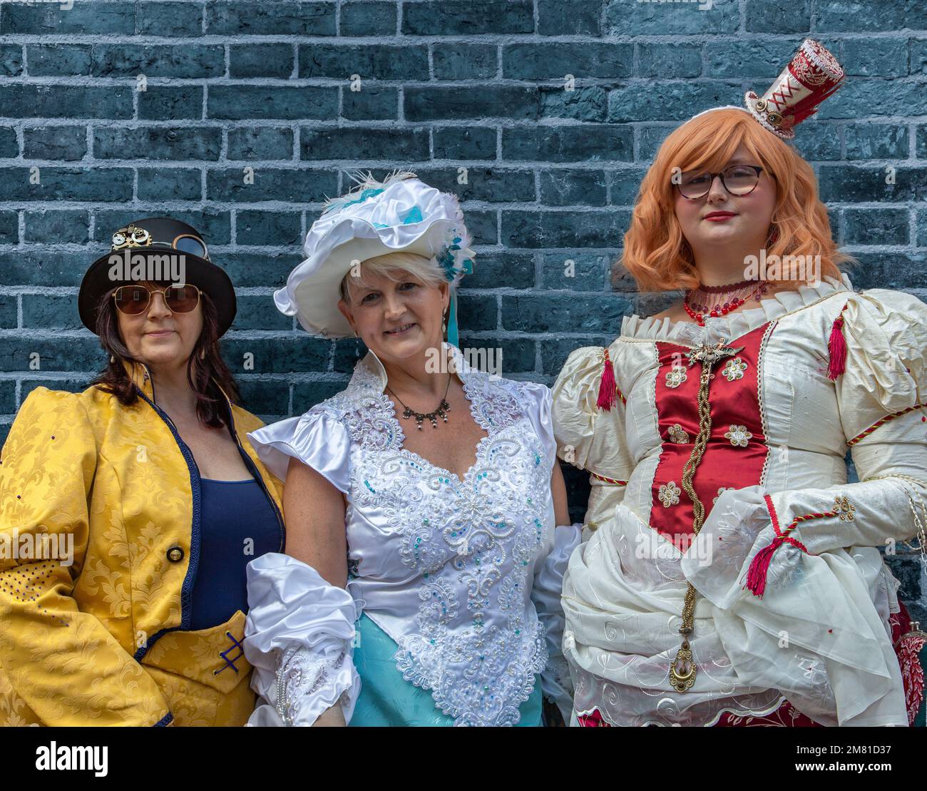 Portrait of three women, female steampunks, smiling while standing next to a wall. Dressed in period costume, steampunk clothing. Stock Photo