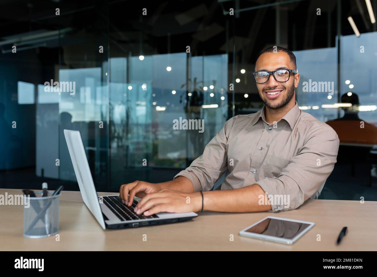 Portrait of successful hispanic businessman inside office, man with laptop working typing on keyboard smiling and looking at camera. Stock Photo