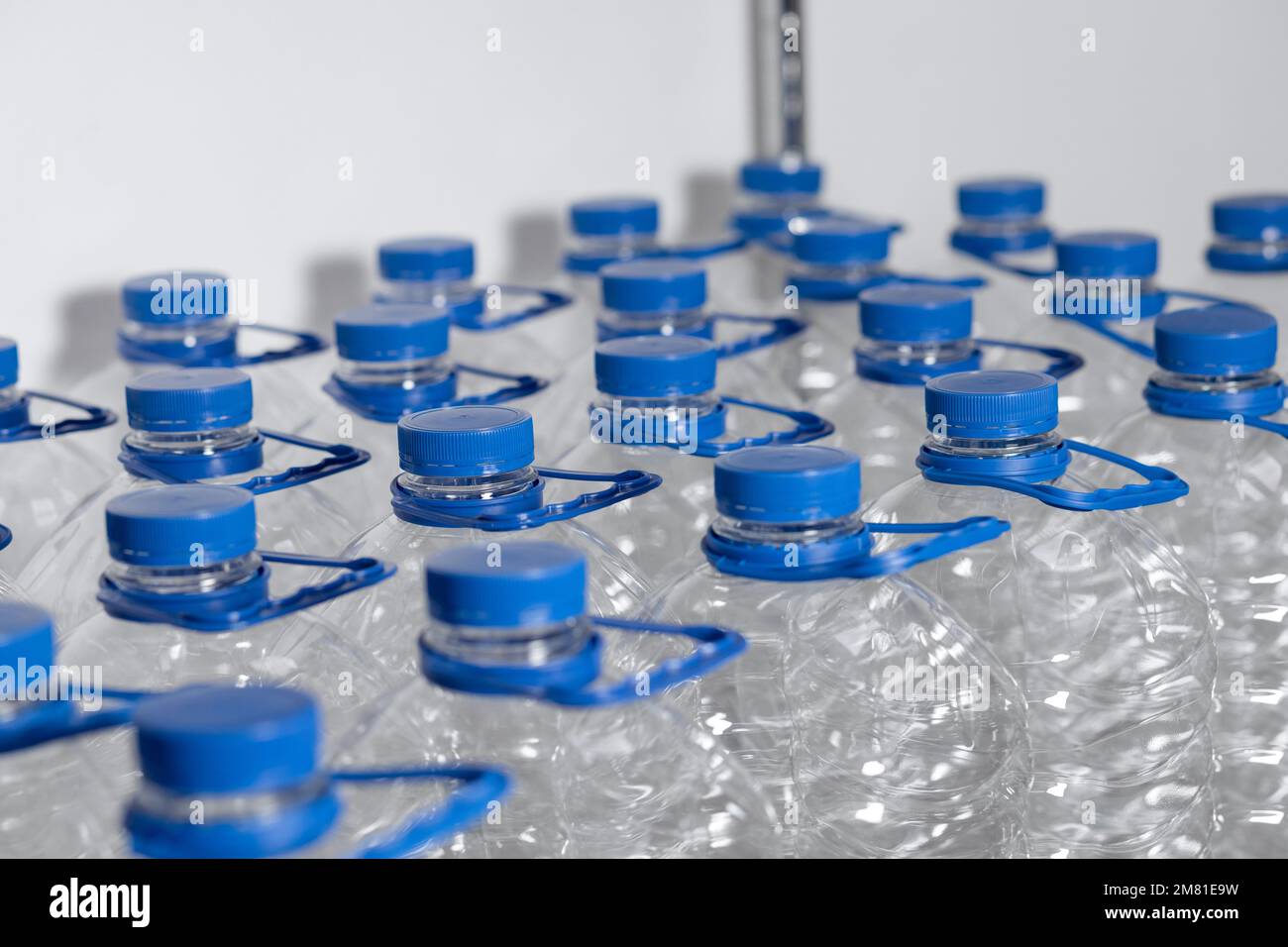 Many empty water bottles with lids and handles are lined up in a