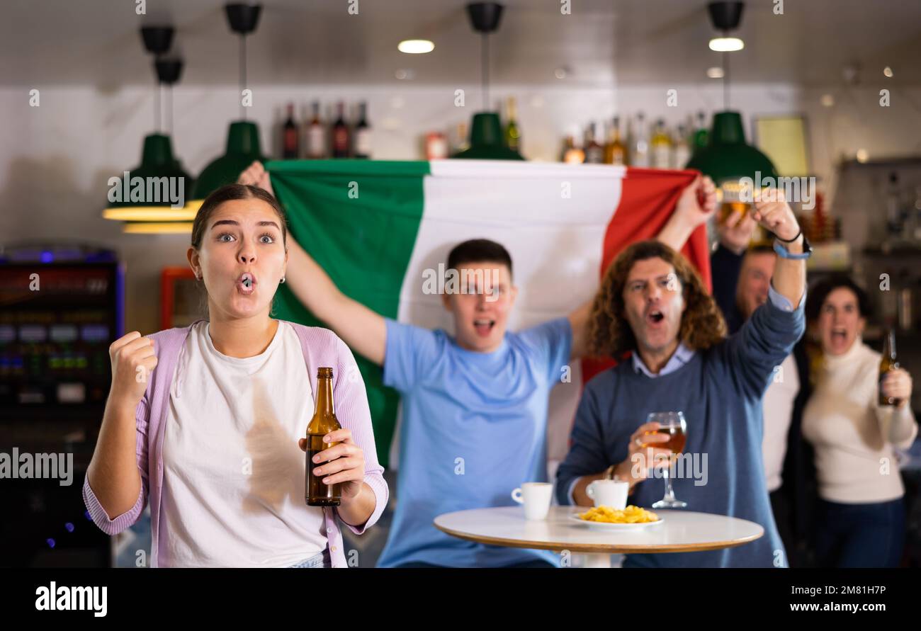 Emotional young adult sports fans waving Italian flag while drinking