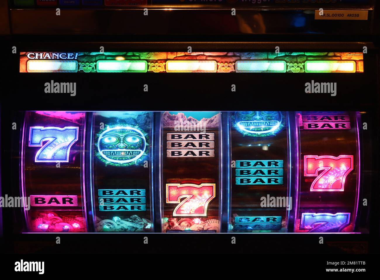 Illuminated slot machine wheels attract players with their colourful graphics and flashing sequences in dimly lit amusement arcacdes. Stock Photo