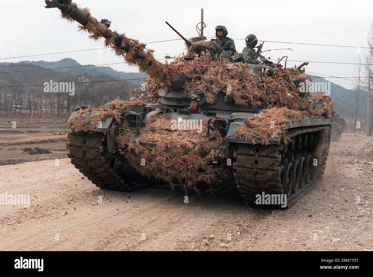 A heavily camouflaged M-48 main battle tank moves down the road with Korean soldiers aboard during the joint South Korean/US Exercise Team Spirit '84. Subject Operation/Series: Team Spirit '84 Country: Republic Of Korea (KOR) Stock Photo