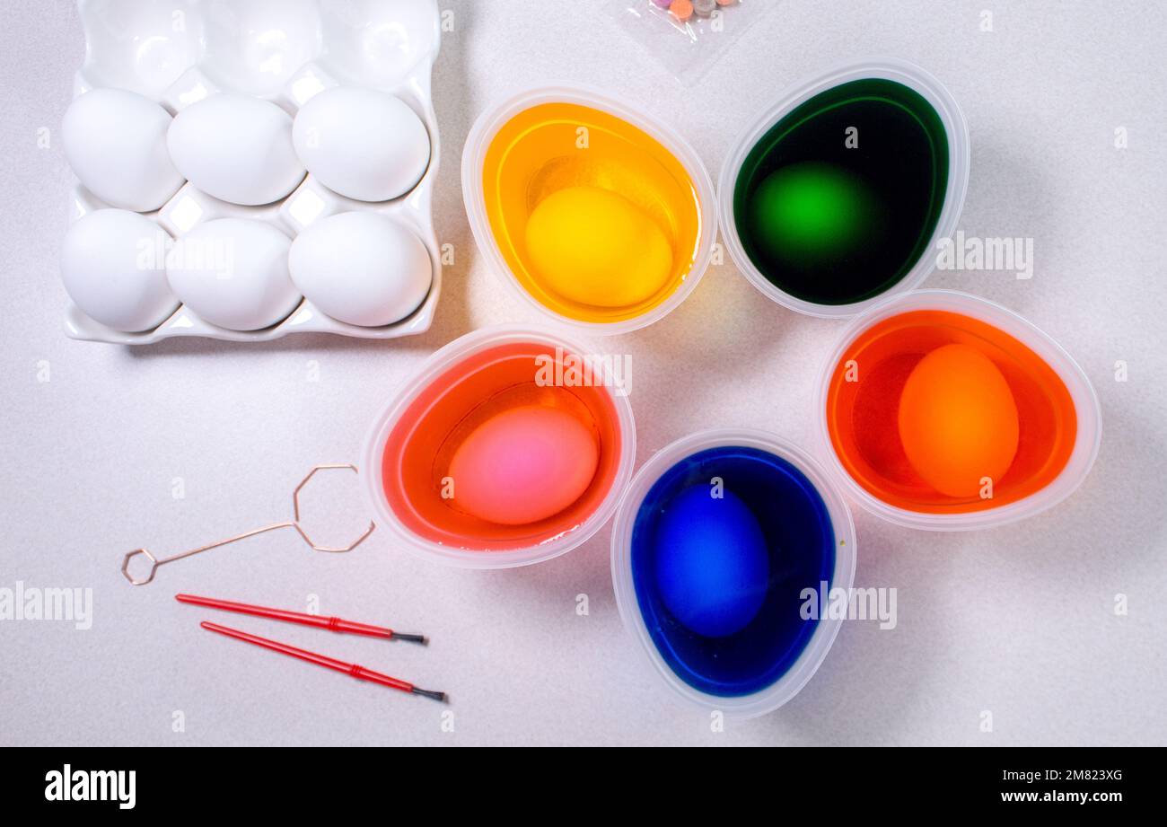 Dyeing easter eggs. Tools for painting eggs for easter, eggs box, cups of colorful paint, easter eggs, plate, brushes and paints on the table side vie Stock Photo