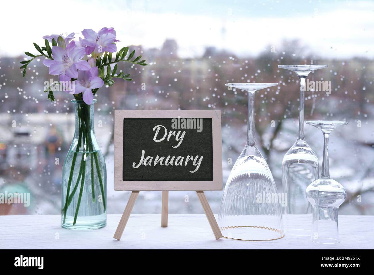 Dry January, month without alcohol. Text Dry January on blackboard, chalk board. Empty vine and beer drinking glasses, freesia flowers. Window with Stock Photo