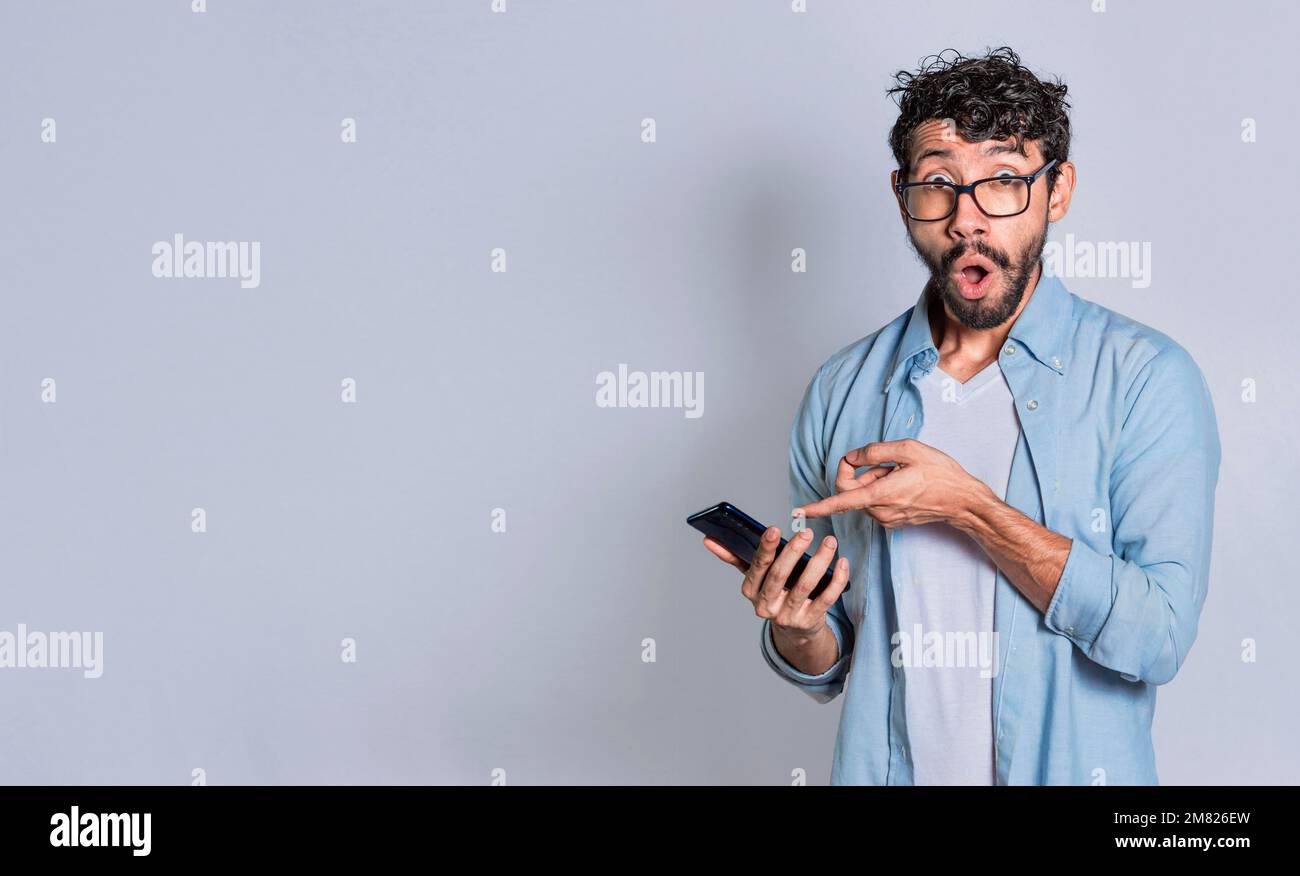 Amazed handsome man pointing at his cell phone isolated, surprised person pointing at his cell phone isolated. Isolated teenager surprised of a Stock Photo