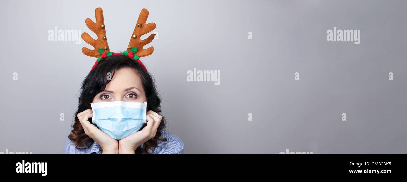Woman wearing protection face mask against coronavirus. Woman in a mask and deer horns headband. Funny Christmas accessory. Medical mask, Close up sho Stock Photo
