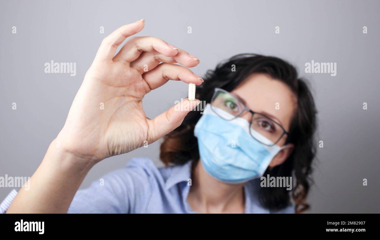 Woman wearing protection face mask against coronavirus and glasses. Woman in a mask showing medicine pill, vaccine. Medical mask, Close up shot, Selec Stock Photo