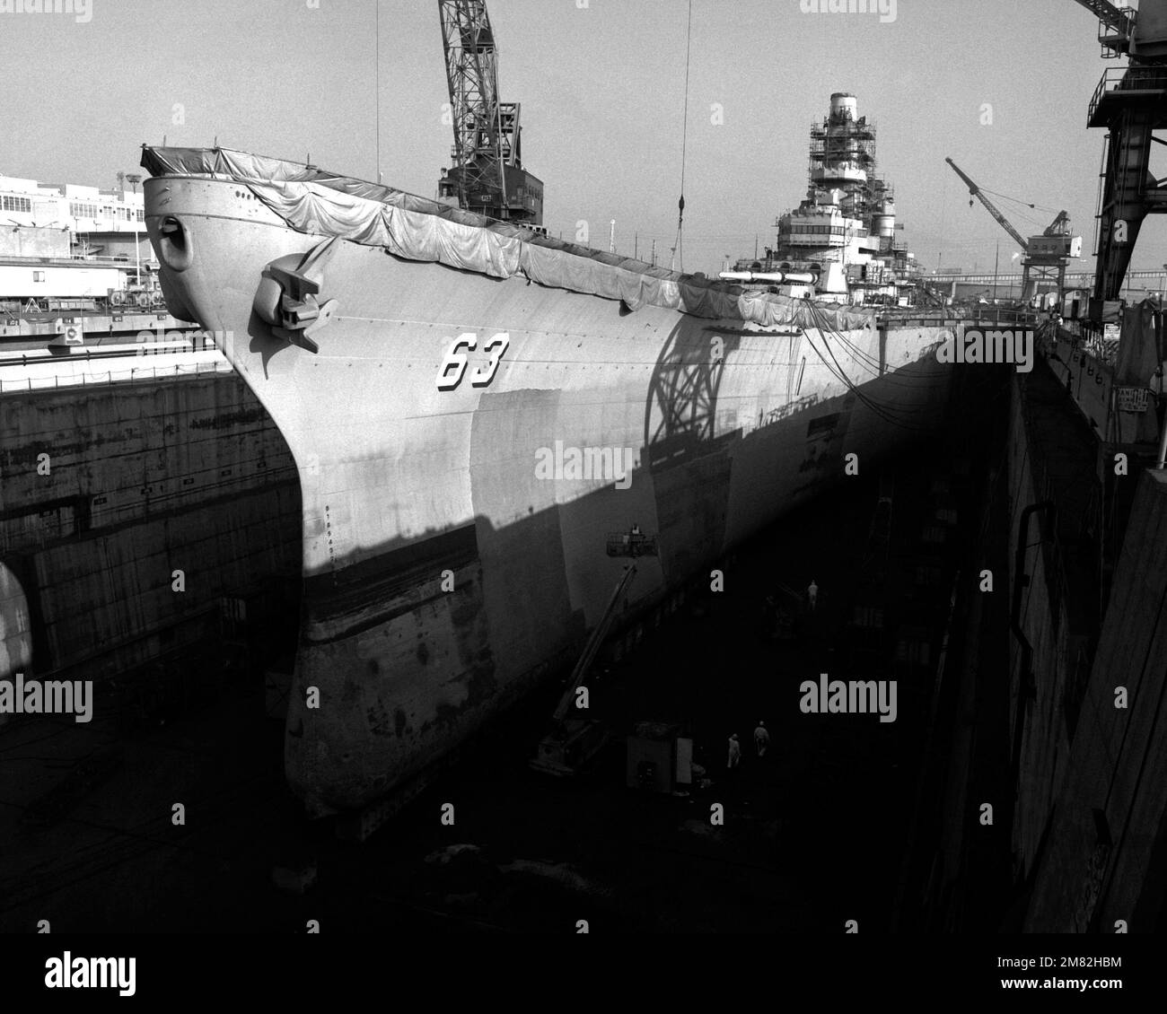 Workers paint the hull of the battleship MISSOURI (BB-63) in dry dock ...