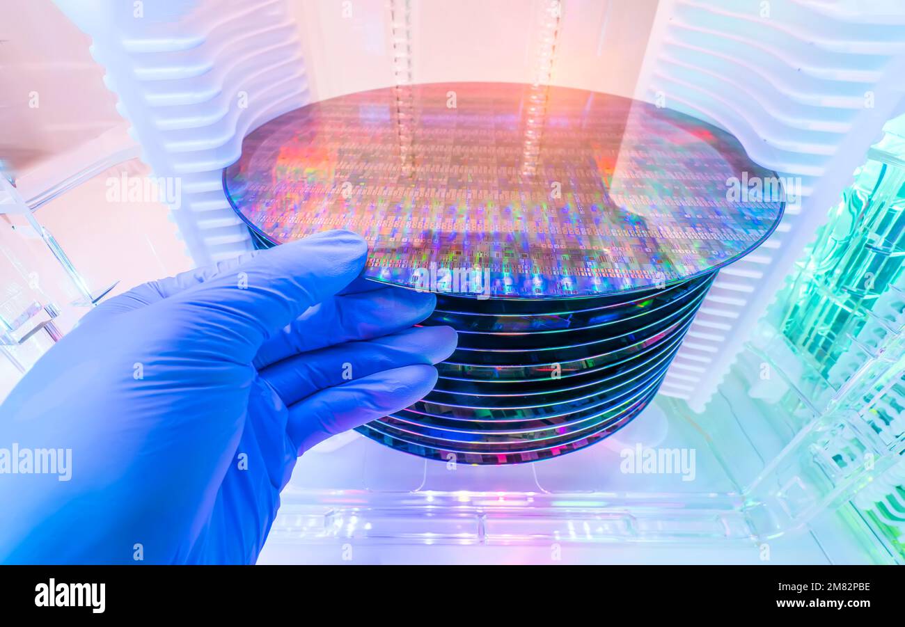 Gloved Hand Holding a Silicon Wafer in plastic holder box used in electronics for the fabrication of integrated circuits Stock Photo
