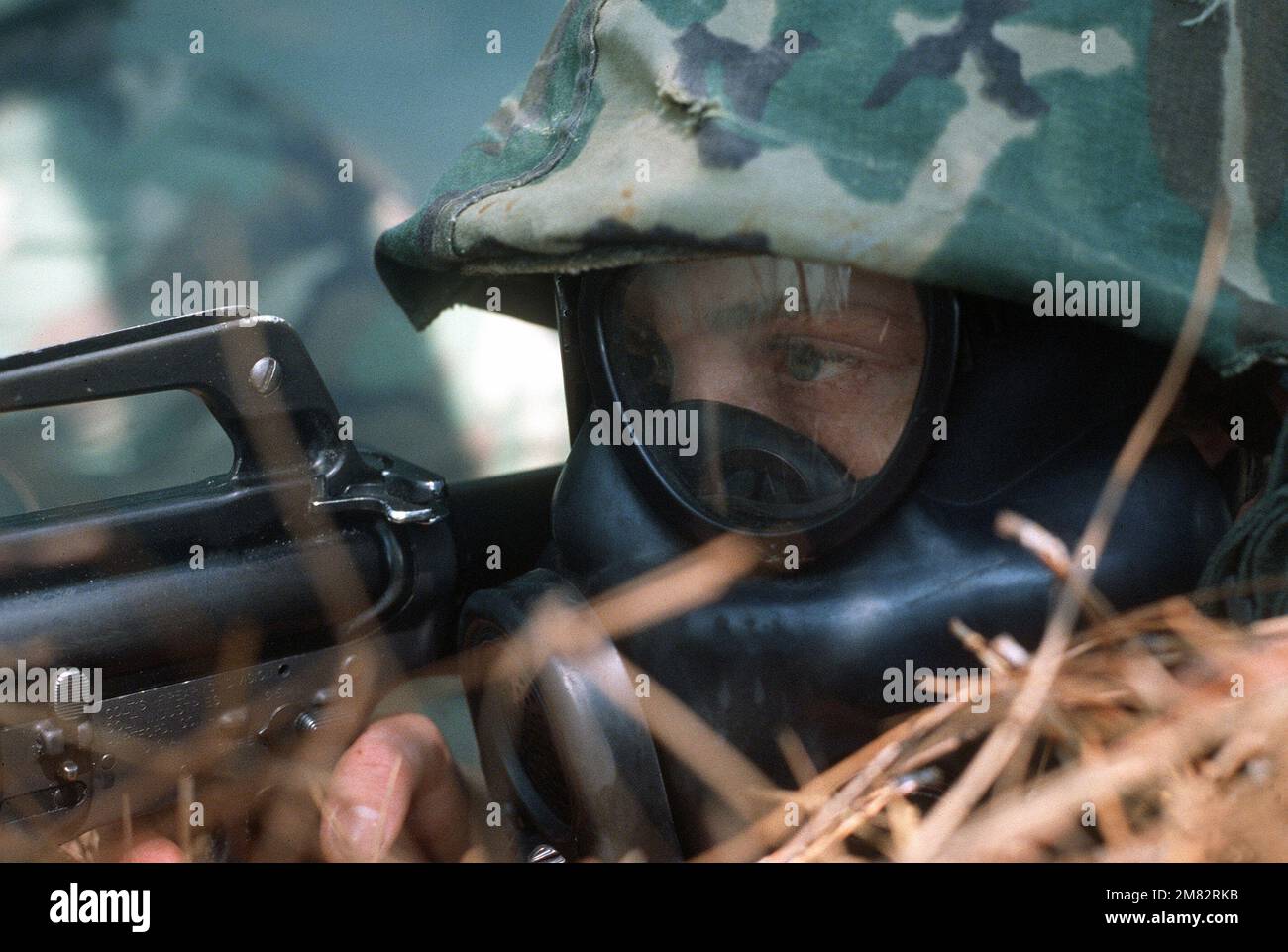 A recruit, wearing an ABC-M17 chemical-biological mask, aims an M-16A1 ...