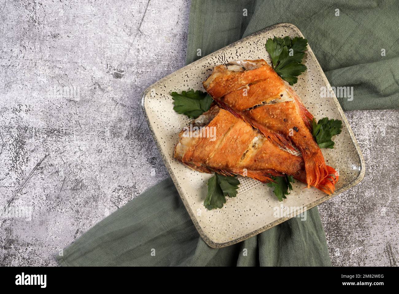 Pan Fried Rose fish with herbs on a square plate on a dark background