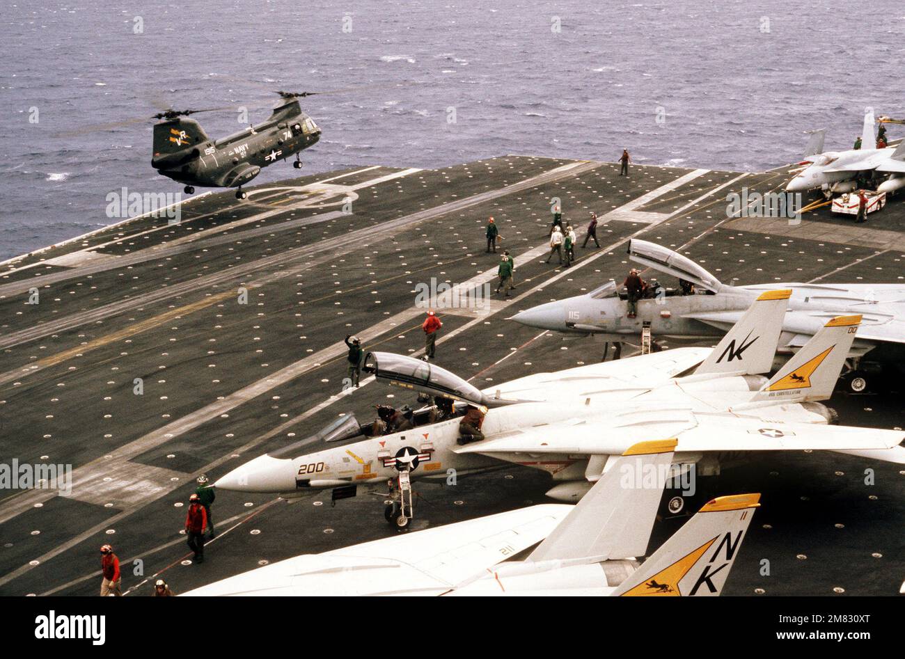 A UH-46D Sea Knight helicopter from the ammunition ship USS KISKA (AE 35) hovers above the flight deck of the aircraft carrier USS CONSTELLATION (CV 64) during Fleet Exercise 85. In the foreground are several F-14A Tomcat aircraft from Fighter Squadron 21. On the far right is an F/A-18A Hornet aircraft. Country: Pacific Ocean (POC) Stock Photo