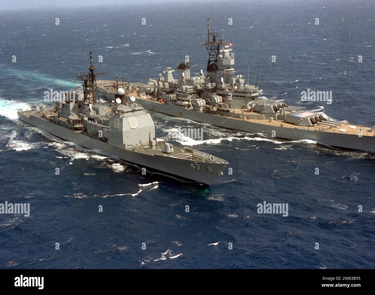 An aerial starboard bow view of the Ticonderoga Class Aegis guided missile cruiser USS TICONDEROGA (CG-47) being refueled by the battleship USS IOWA (BB-61), background. The ships, part of Commander Task Group 28.6, are underway off the coast of Costa Rica. Country: Caribbean Sea Stock Photo