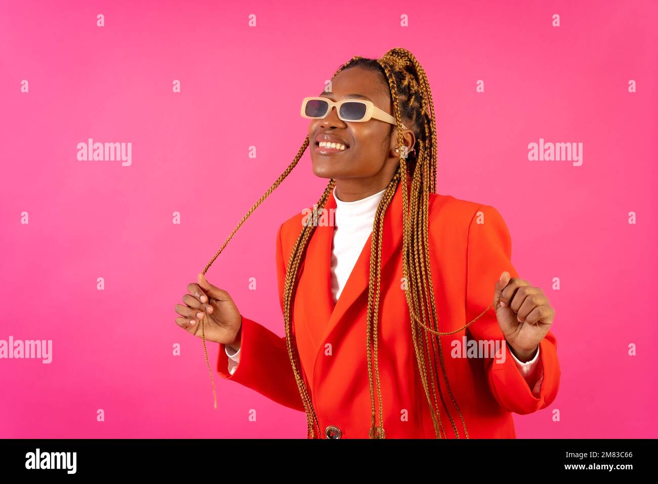An African young woman with braids posing and smiling on a pink ...