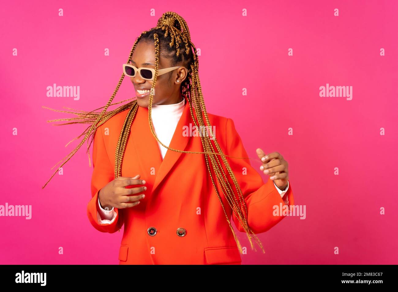An African young woman with braids posing and smiling on a pink ...