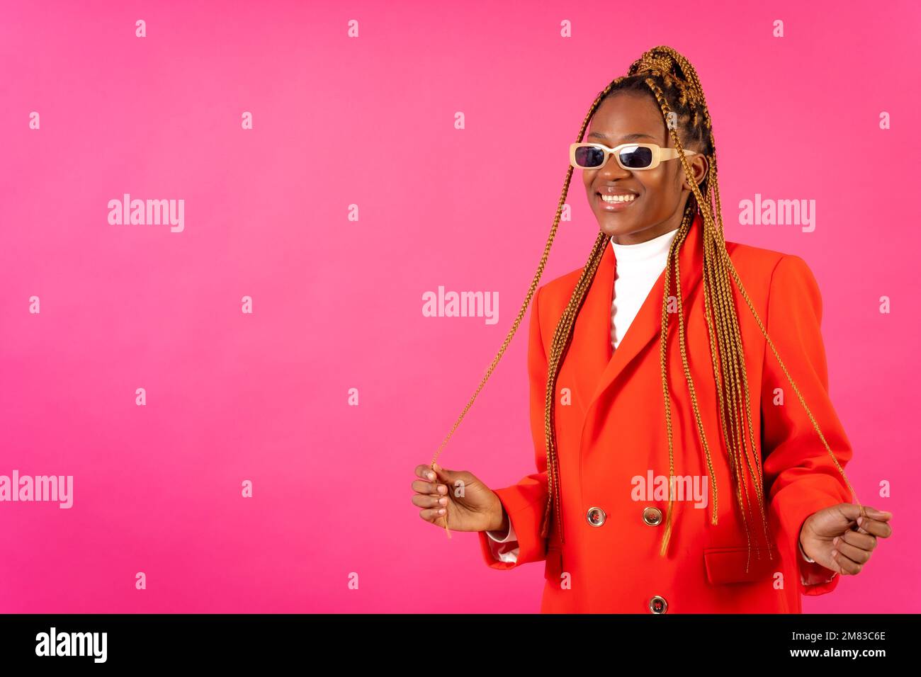 An African young woman with braids posing and smiling on a pink ...