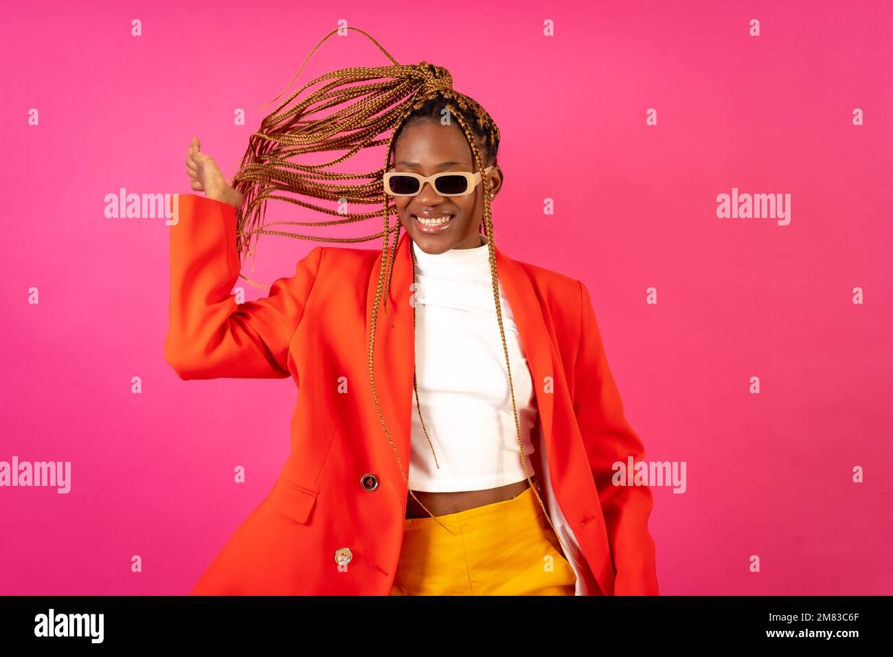 An African young woman with braids posing and smiling on a pink ...