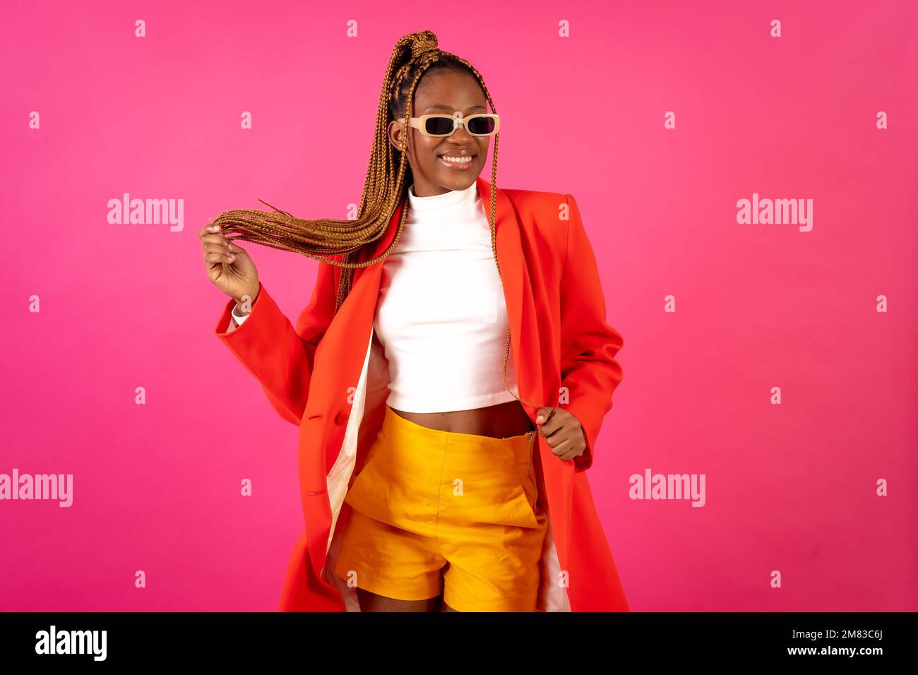 An African young woman with braids posing and smiling on a pink ...