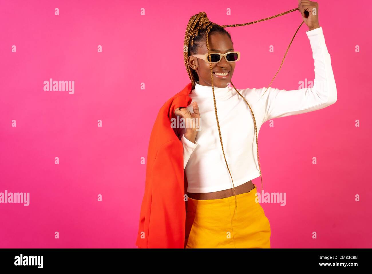 An African young woman with braids posing and smiling on a pink ...