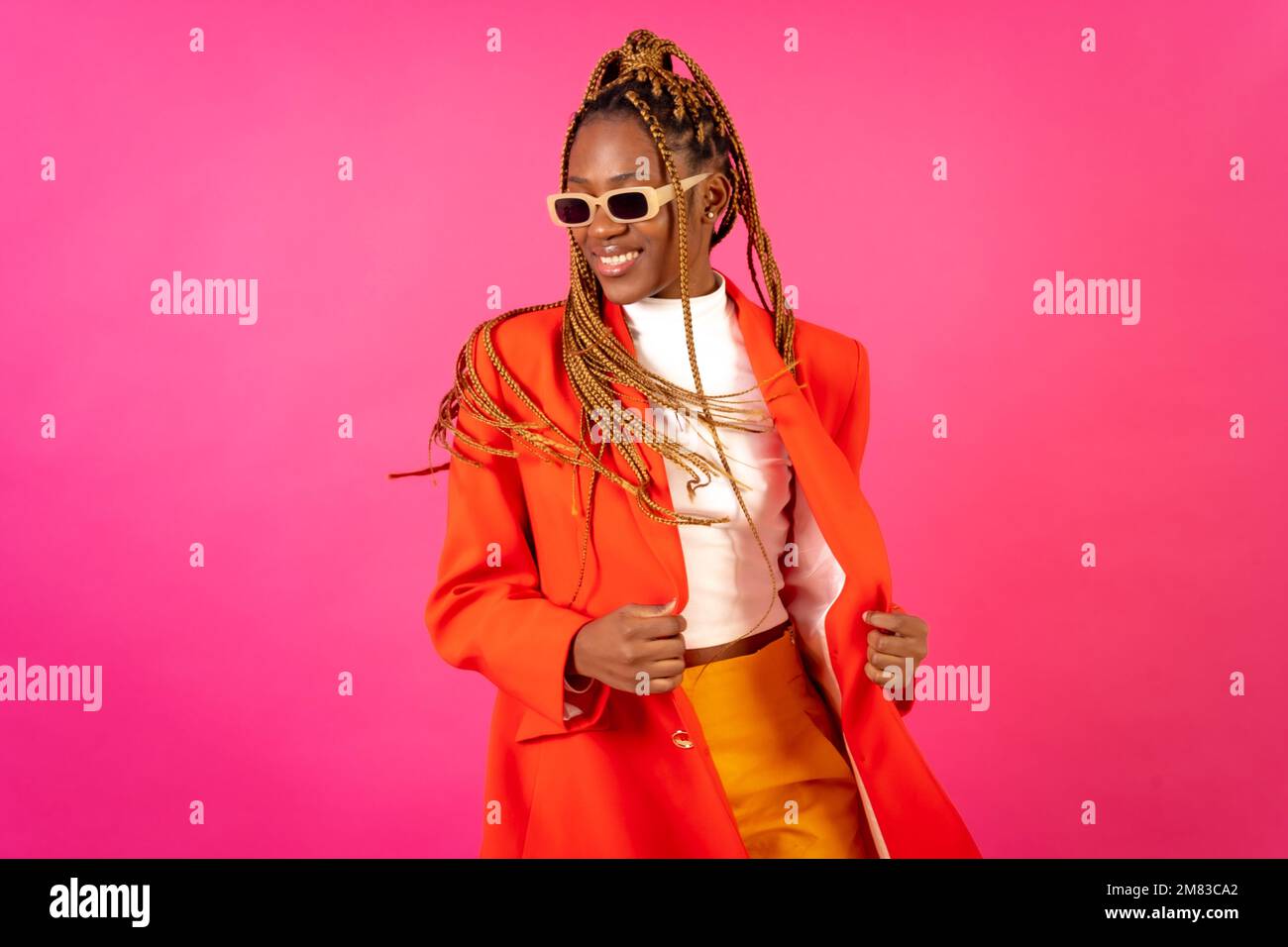 An African young woman with braids posing and smiling on a pink ...