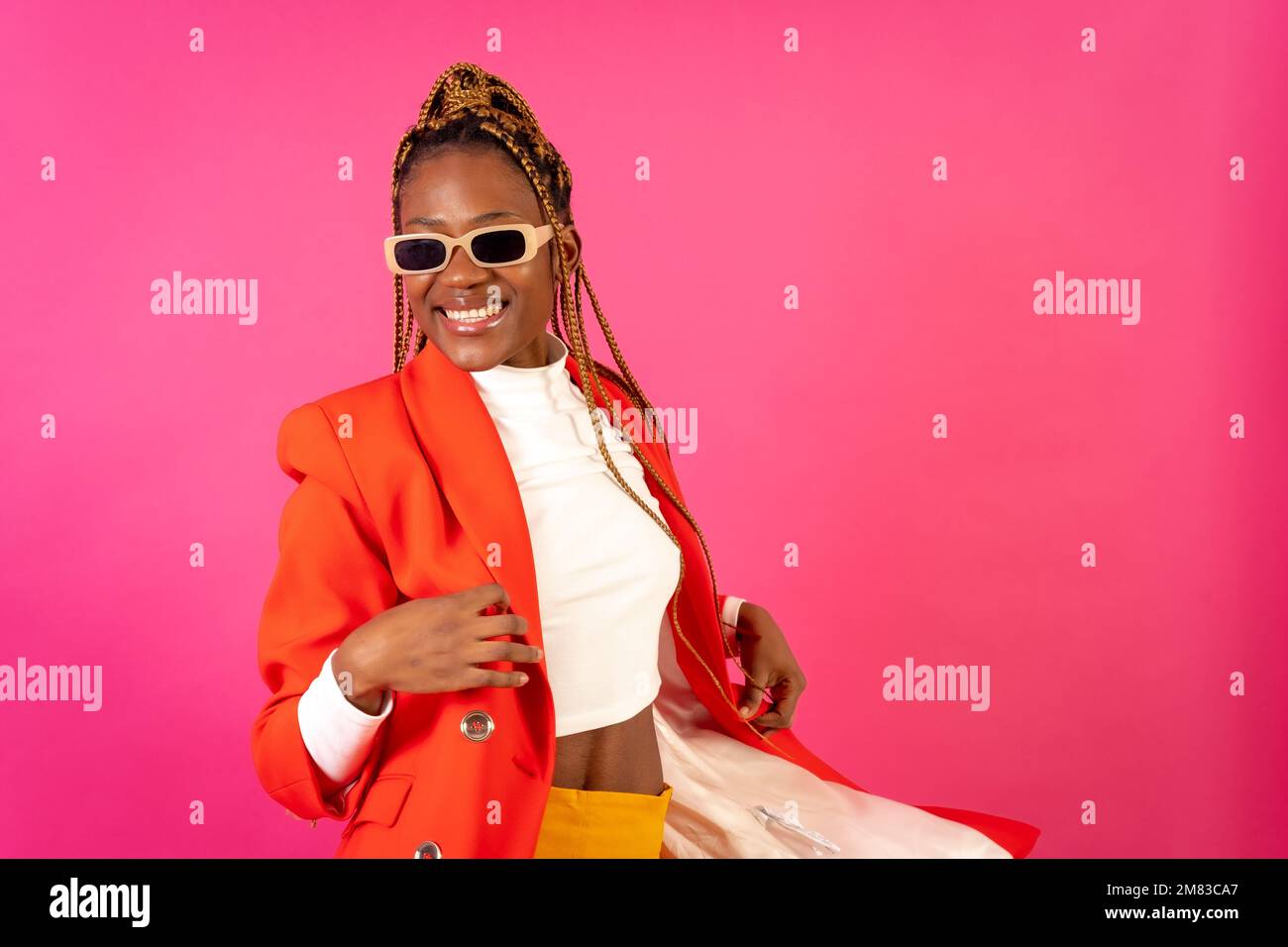 An African young woman with braids posing and smiling on a pink ...