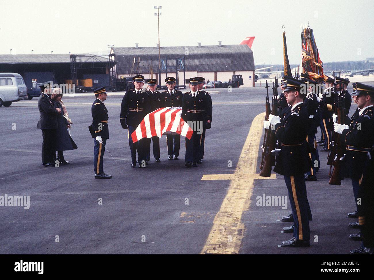 Members of a U.S. Army honor guard and color guard stand at attention as pallbearers carry the casket of MAJ. Arthur D. Nicholson Jr. to an aircraft during a departure ceremony in his honor. Nicholson was shot and killed while on duty in East Berlin. Standing on the left are his widow, Karyn, and daughter Jennifer. Base: Rhein-Main Air Base Country: Deutschland / Germany (DEU) Stock Photo