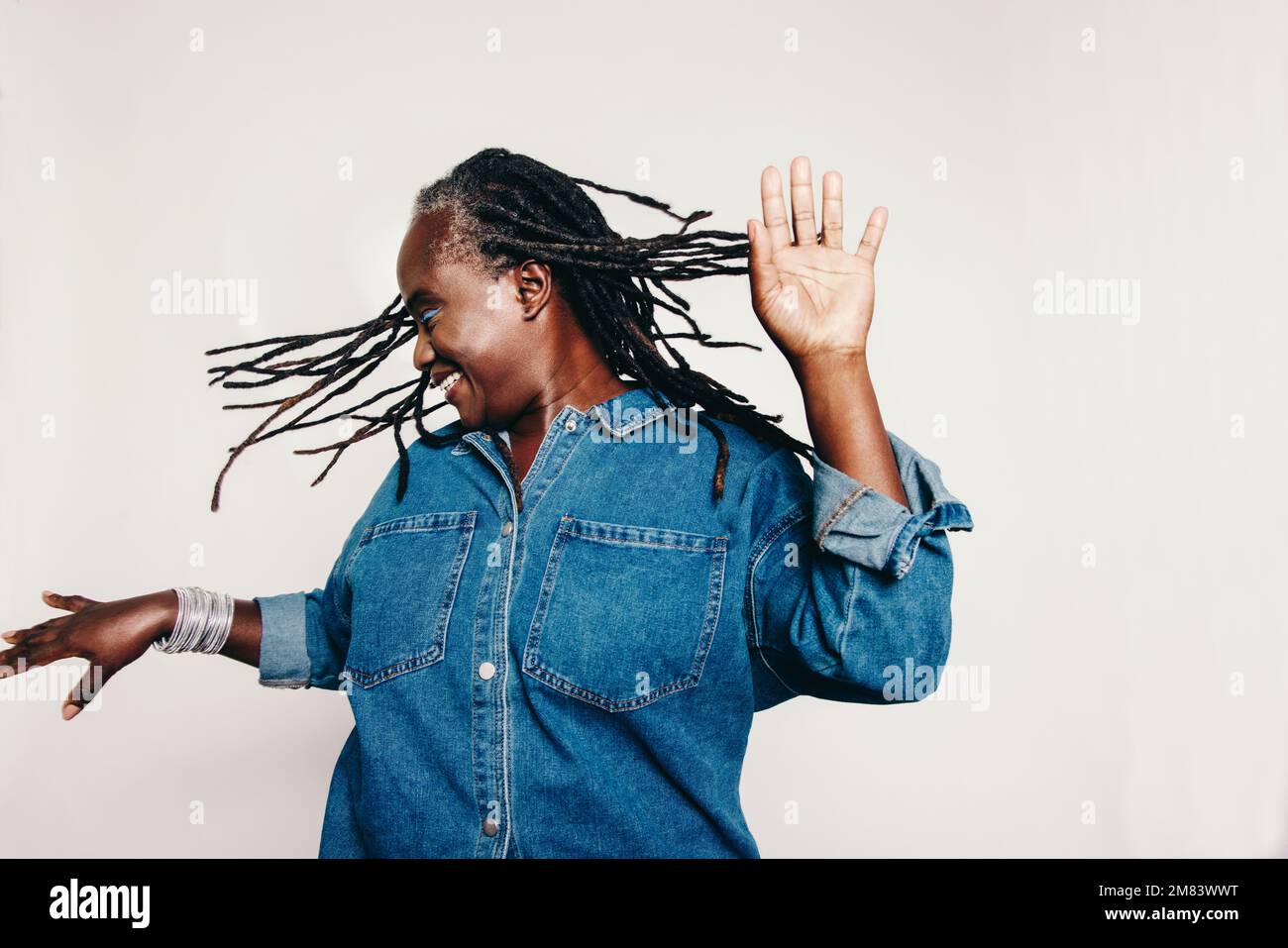 Fun with dreadlocks. Happy mature woman dancing and whipping her hair while standing against a grey background. Cheerful middle-aged woman wearing a d Stock Photo