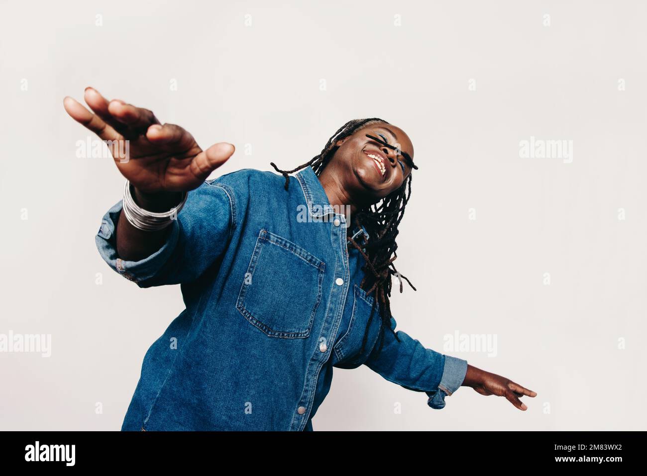 Happy woman having fun in the studio. Carefree woman with dreadlocks smiling with her eyes closed and her arms outstretched. Cheerful mature woman wea Stock Photo