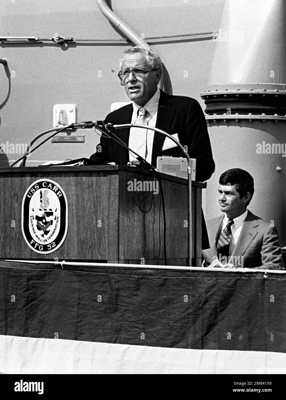 Jack Yusen, SAMUEL B. ROBERTS (DD-413) Survivors Association representative, addresses guests at the commissioning of the guided missile USS CARR (FFG-52). John T. Gilbride Jr., vice president and general manager, Todd Seattle, is seated in the background. Base: Seattle State: Washington (WA) Country: United States Of America (USA) Stock Photo
