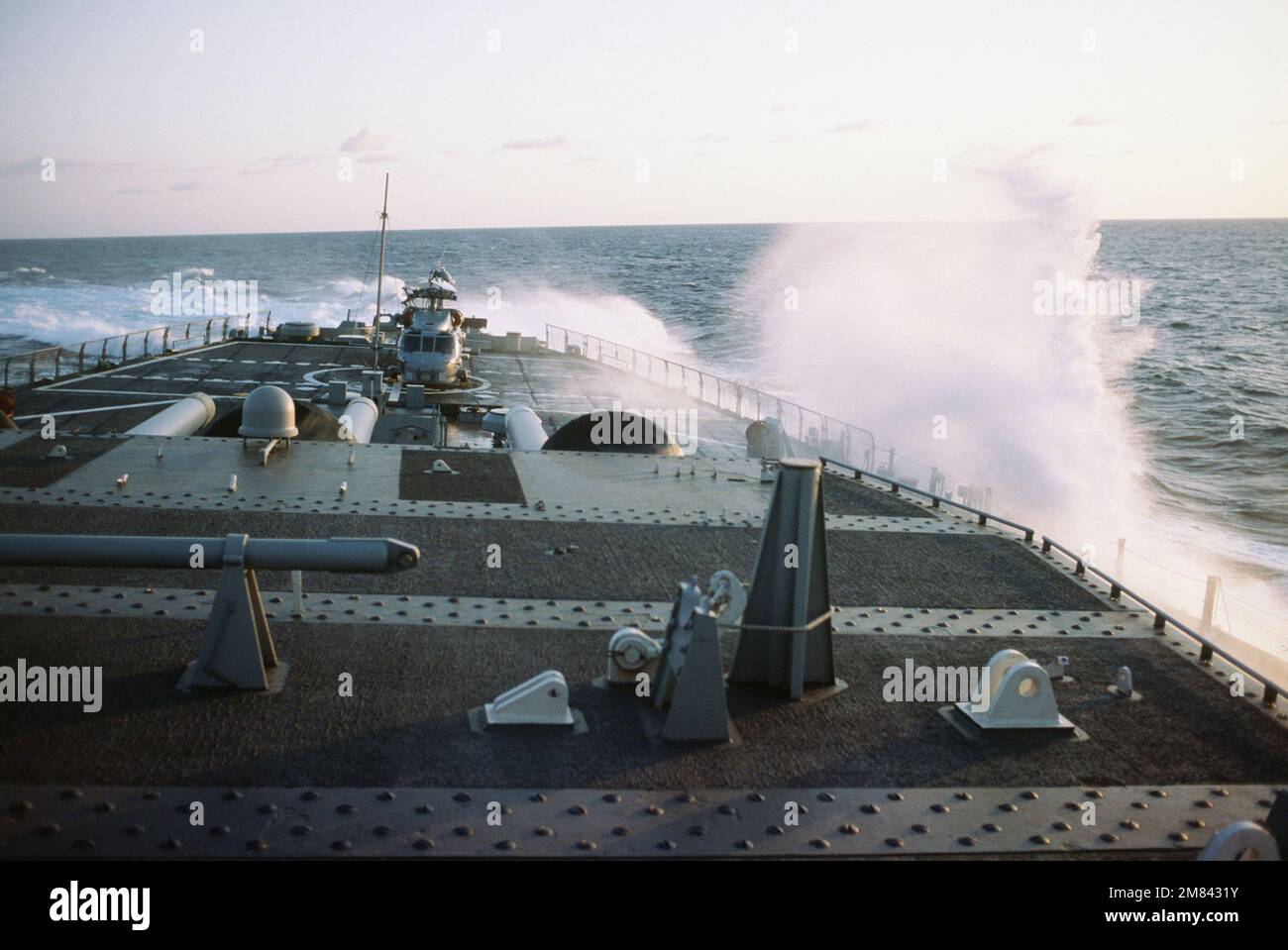 The battleship USS IOWA (BB 61) steers sharply to starboard causing a breaker to crash onto the ship's helicopter pad. An SH-60B Sea Hawk helicopter is parked on the pad with rotor blades folded. Base: USS Iowa (BB 61) Country: Atlantic Ocean (AOC) Stock Photo