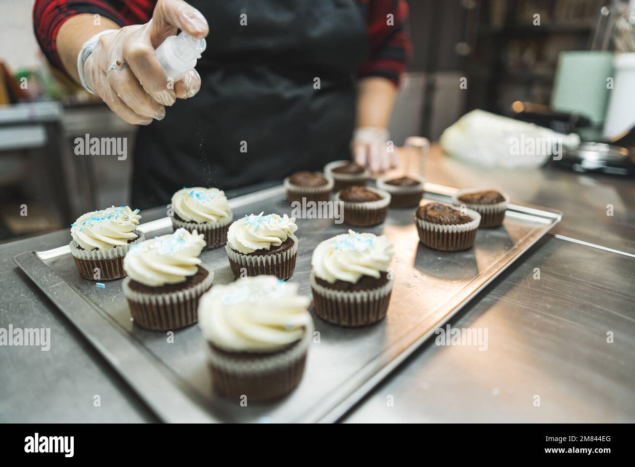 baker adding light blue sprinkles to the whipped cream cupcakes at the bakery, baking concept. High quality photo Stock Photo
