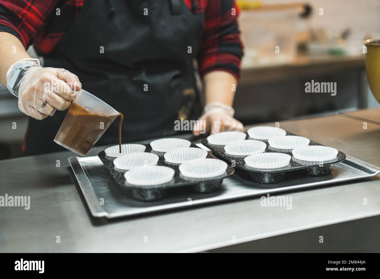 closeup view of female chef with gloves putting dough from a mug to paper cups for muffins. High quality photo Stock Photo