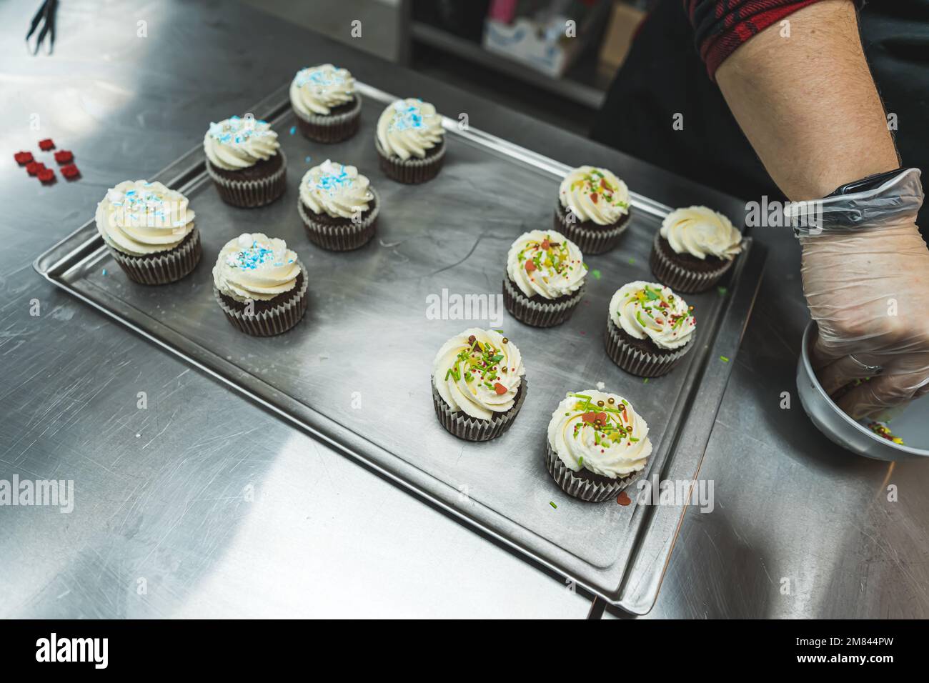 a baker adding sprinkles to the chocolate cupcakes with whipped cream, preparing for Christmas. High quality photo Stock Photo