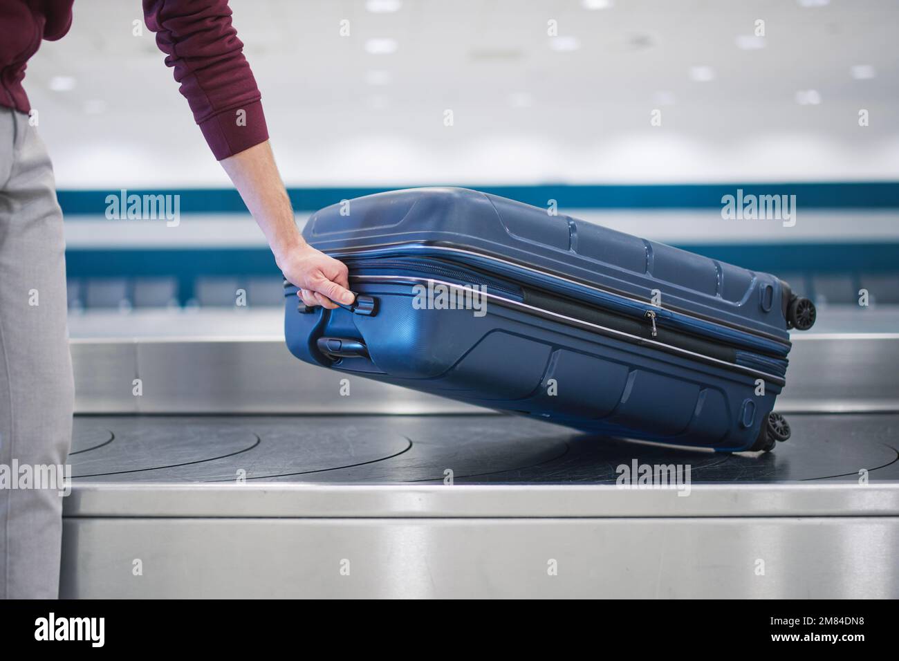 Traveling by airplane. Passenger pick up his blue suitcase in baggage