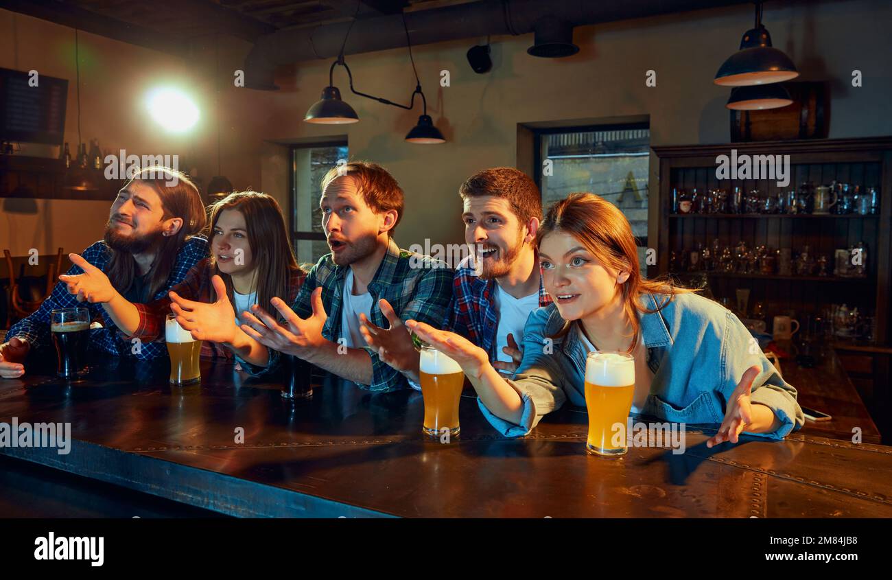 Friends meeting. Young people, men and women watching match at pub. Fans emotionally cheering up favourite sport team. Drinking beer Stock Photo