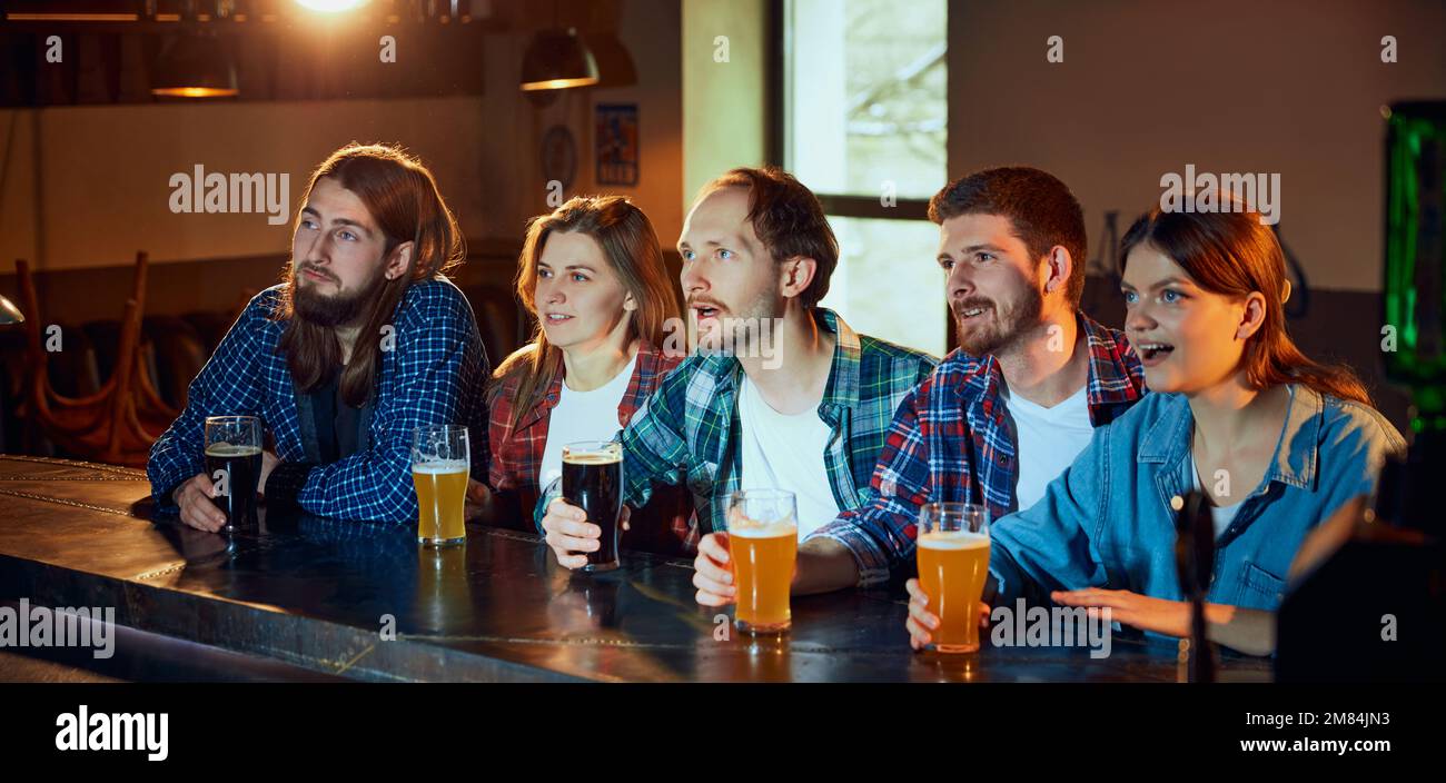 Friends, young people, men and women watching match at pub. Fans emotionally watching sport competition Stock Photo
