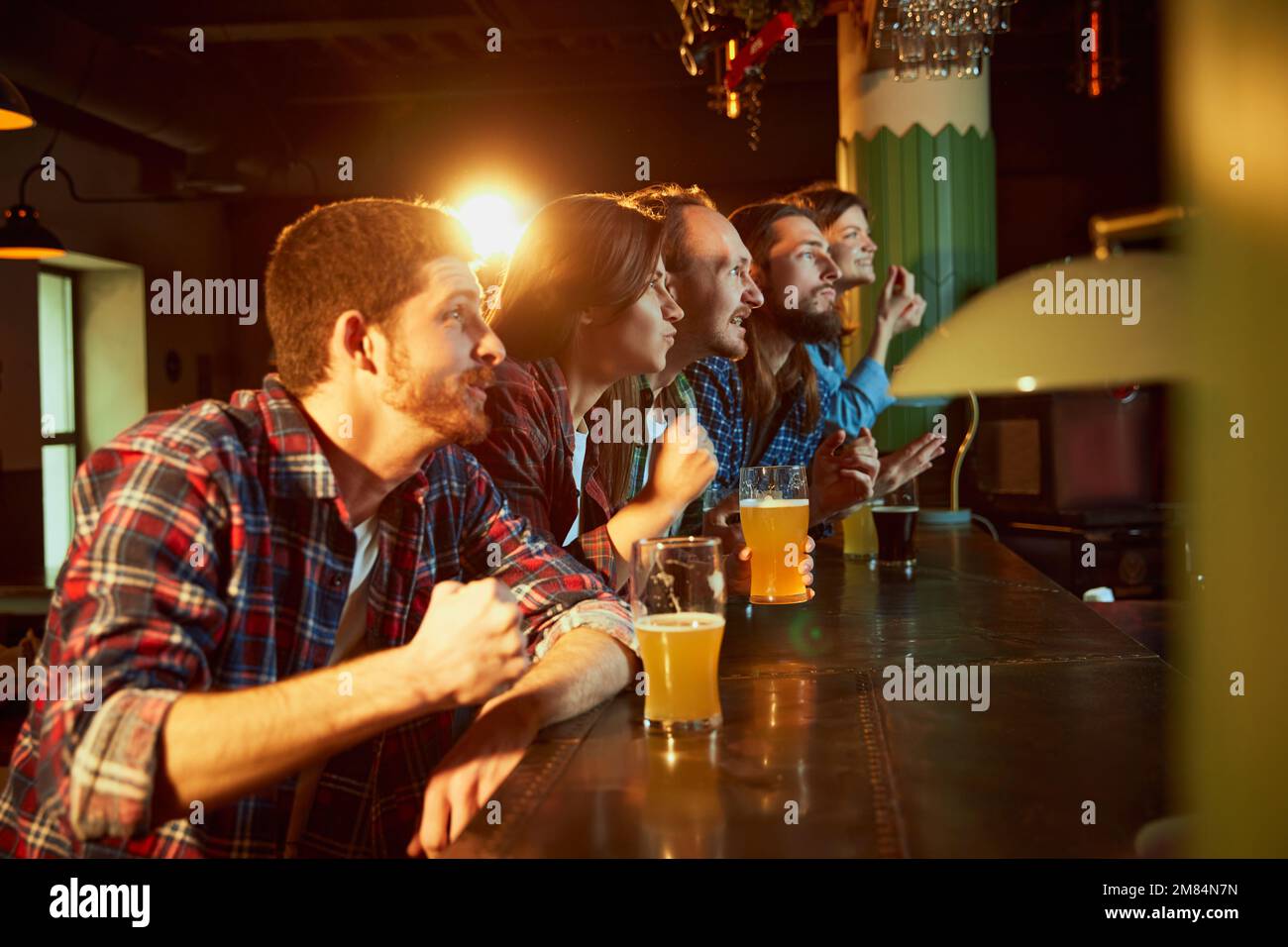 Young people, friends meeting to watch match at pub and drink beer. Fans emotionally cheering up favourite sport team. Winning moment Stock Photo