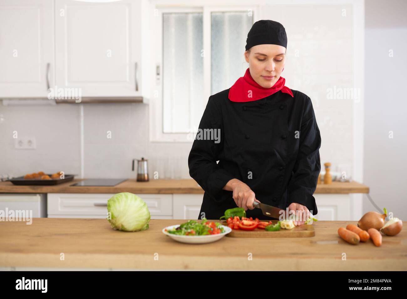 Female cook in black uniform chopping vegetables in kitchen Stock Photo