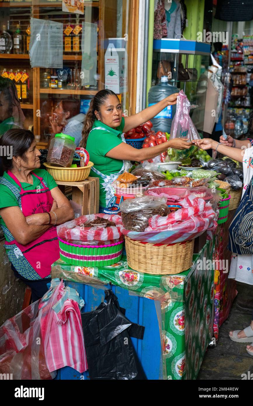A woman sells fresh produce in the Benito Juarez Market in the historic center of Oaxaca, Mexico.  In front is a woman selling chapulines or roasted g Stock Photo