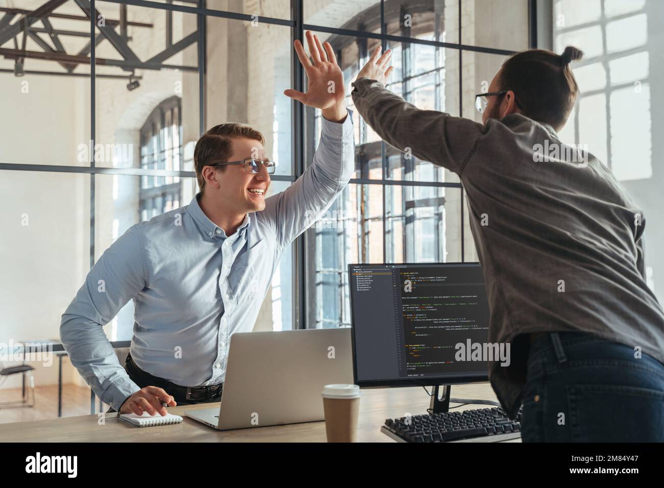 Colleagues coders giving high five to each other celebrating successful start-up launch. Programmers rejoice at the successful launch of their product. Stock Photo
