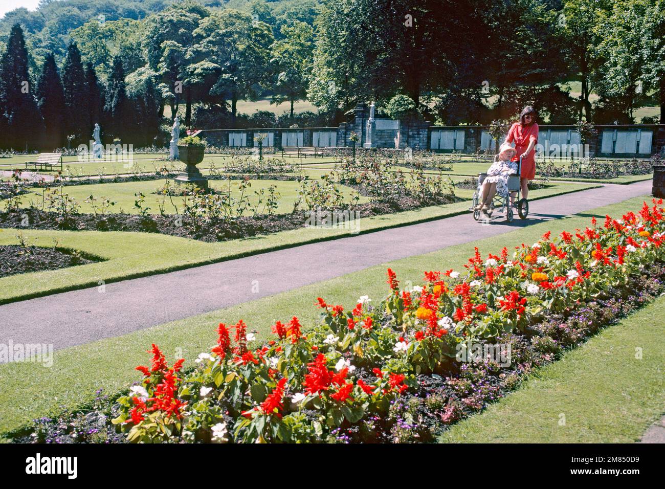 Woman pushing elderly woman in wheelchair through the gardens at Centre Vale Park in 1986, Todmorden, West Yorkshire Stock Photo
