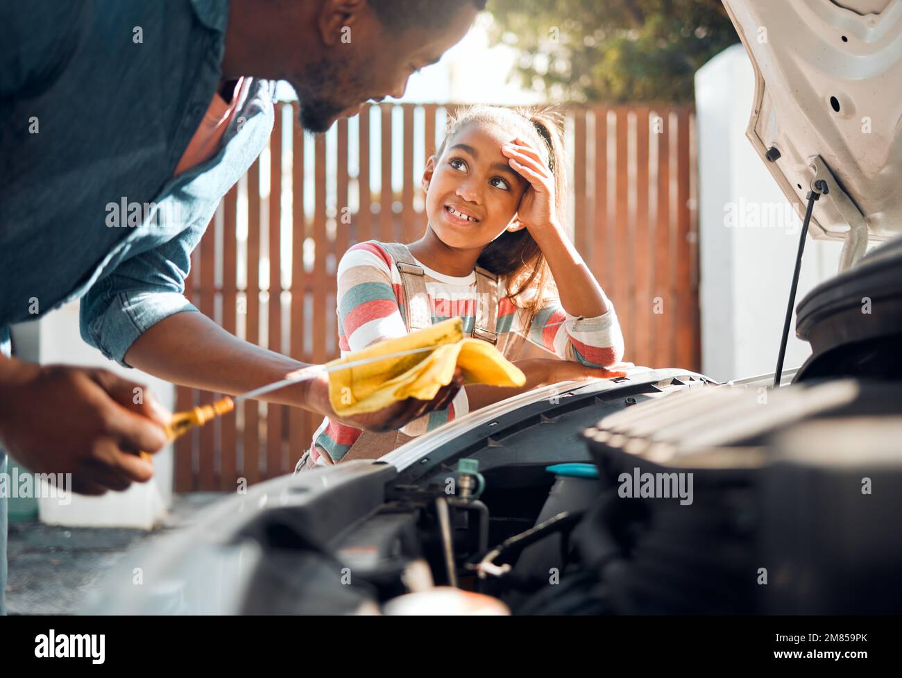 Car problem, child and dad working as a mechanic while teaching daughter to change motor oil and fix vehicle. Black man and girl kid learning, talking Stock Photo