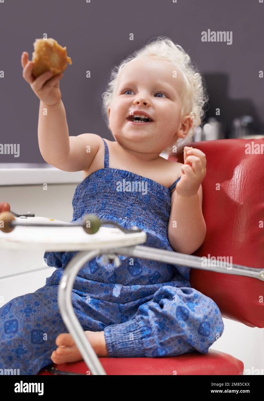 I can feed myself. a cute young baby sitting in a high chair eating. Stock Photo