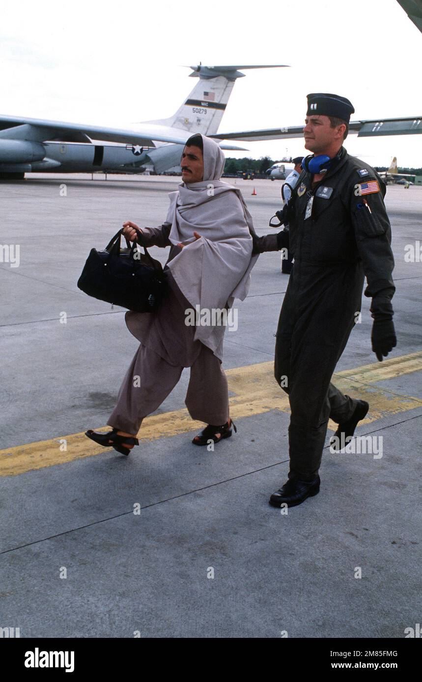 A Military Airlift Command officer escorts an Afghan man from a C-141B Starlifter aircraft to a bus following their arrival on base. The man is one of 25 Afghan civilians being transported to the U.S. Air Force Regional Medical Center at Weisbaden, West Germany, for specialized medical treatment following injuries incurred as a result of Afghanistan's civil war. The patients will later be evacuated to hospitals in Europe and the United States for donated medical assistance. Base: Rhein-Main Air Base Country: Deutschland / Germany (DEU) Stock Photo