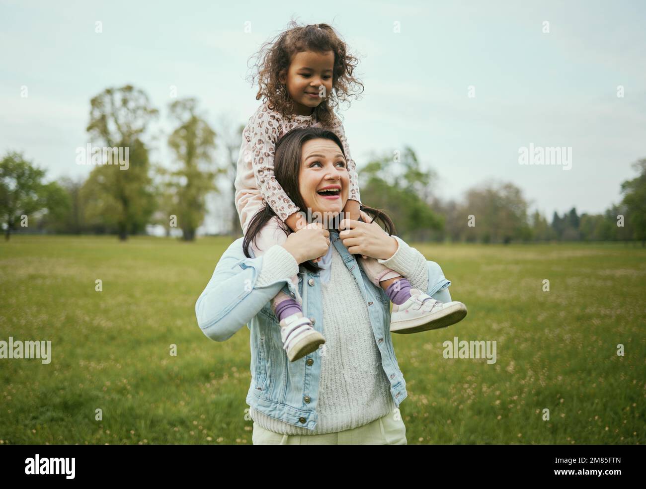 Mother, girl and sitting on shoulders in park for happiness, bonding or care in nature, walk or together outdoor. Woman, child and game on holiday Stock Photo