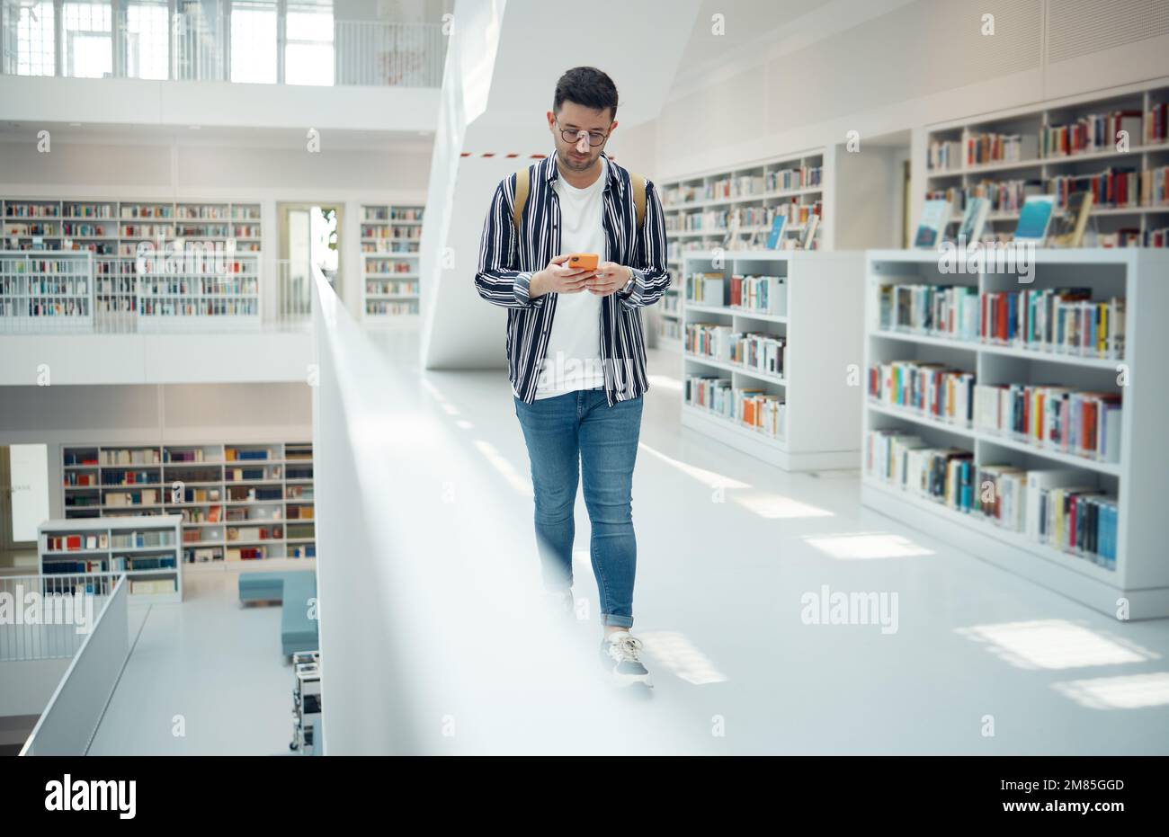 Student walking in library with phone for university, education or college website, internet search and academy faq, about us or contact. Campus Stock Photo