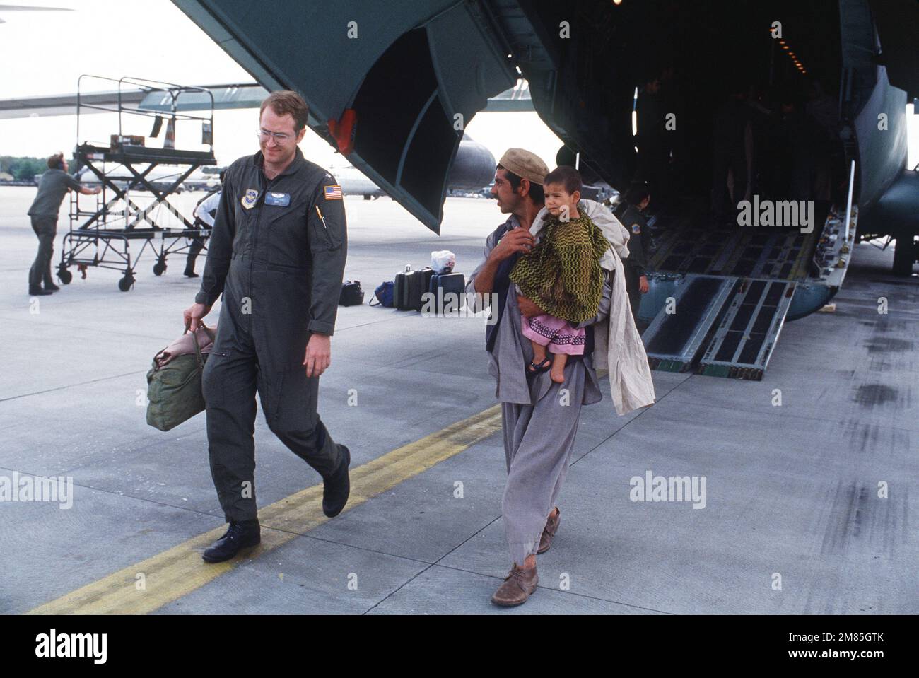 A Military Airlift Command airman escorts an Afghan man and child from a C-141B Starlifter aircraft toward an awaiting bus following their arrival on base. The two are among 25 Afghan civilians being transported to the US Air Force Regional Medical Center at Weisbaden, West Germany, for specialized medical treatment following injuries incurred as a result of Afghanistan's civil war. The patients will later be evacuated to hospitals in Europe and the United States for donated medical assistance. Base: Rhein-Main Air Base Country: Deutschland / Germany (DEU) Stock Photo