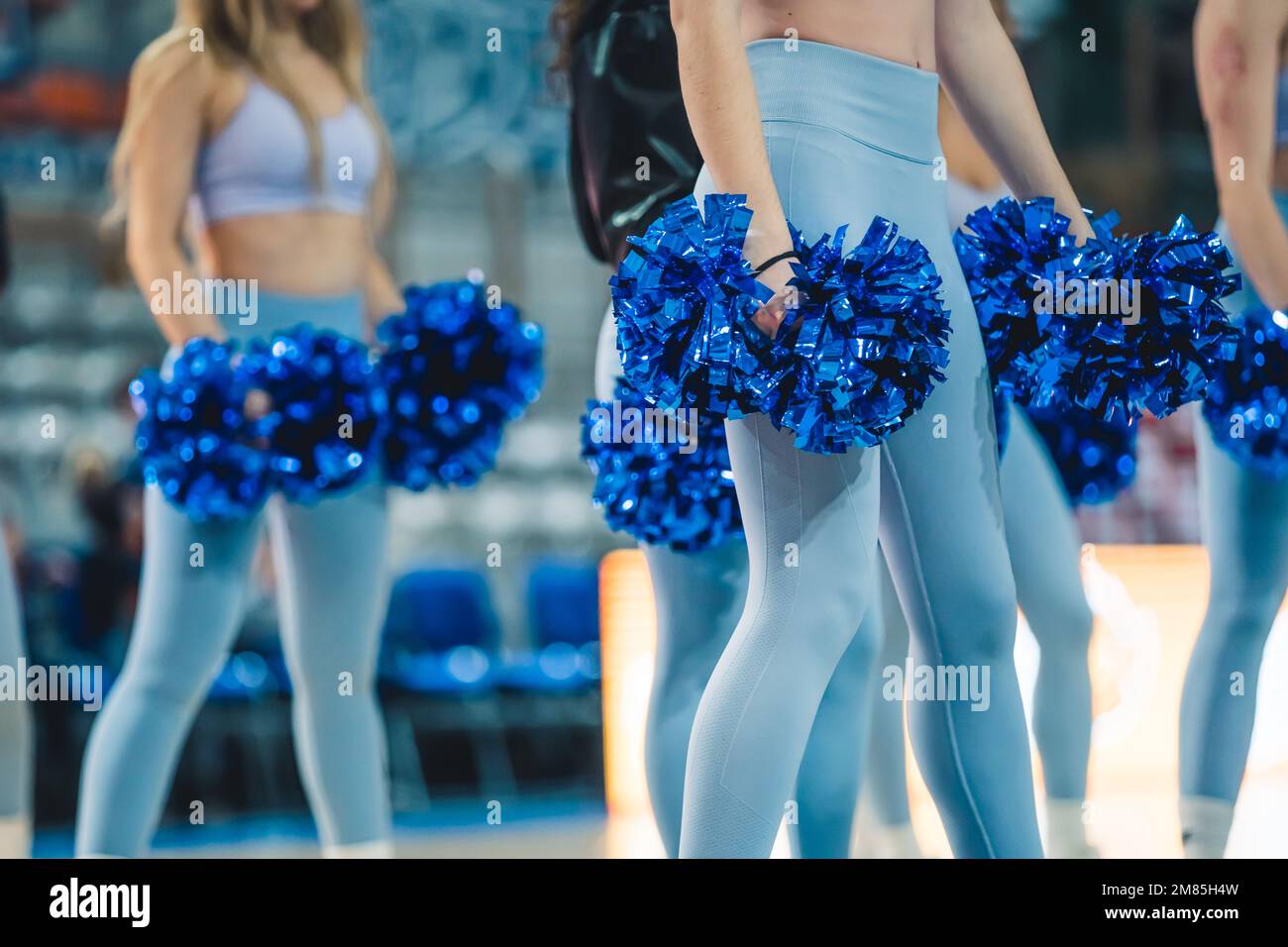 A group of cheerleaders are ready to perform. The cheerleaders are all wearing blue high-waisted tights. Holding pom-poms in their hands adds to the image's energetic and celebratory atmosphere. Stock Photo