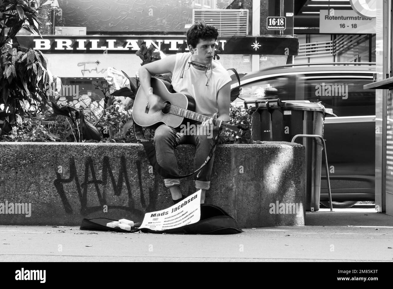 Mads Jacobsen, busker, playing guitar seated on wall near hotdog stand on Rotenturmstrasse in Vienna while couple buy lunch Stock Photo