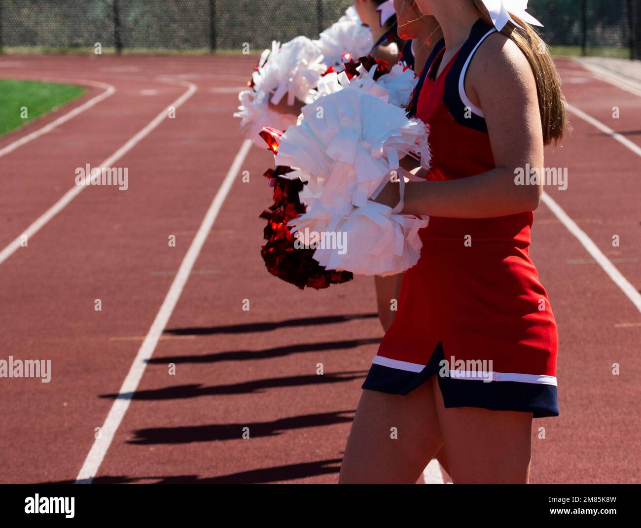 A row of high school cheerleaders holding their pom poms in front on the sidleines of a football game. Stock Photo